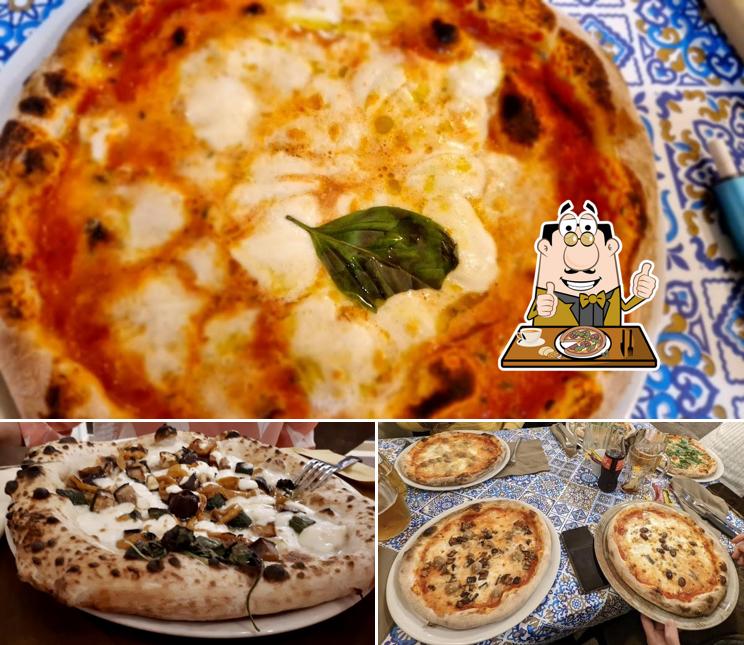 Tre pizze servite insieme su un tavolo coperto di piastrelle in maiolica bianca e blu, con bicchieri e posate